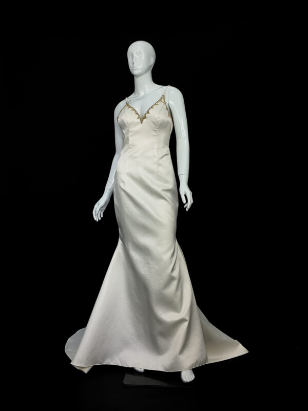 Bride in the Gilded Venus wedding dress, featuring shimmering gold embroidery and a fitted silhouette, posing in a sunlit interior.