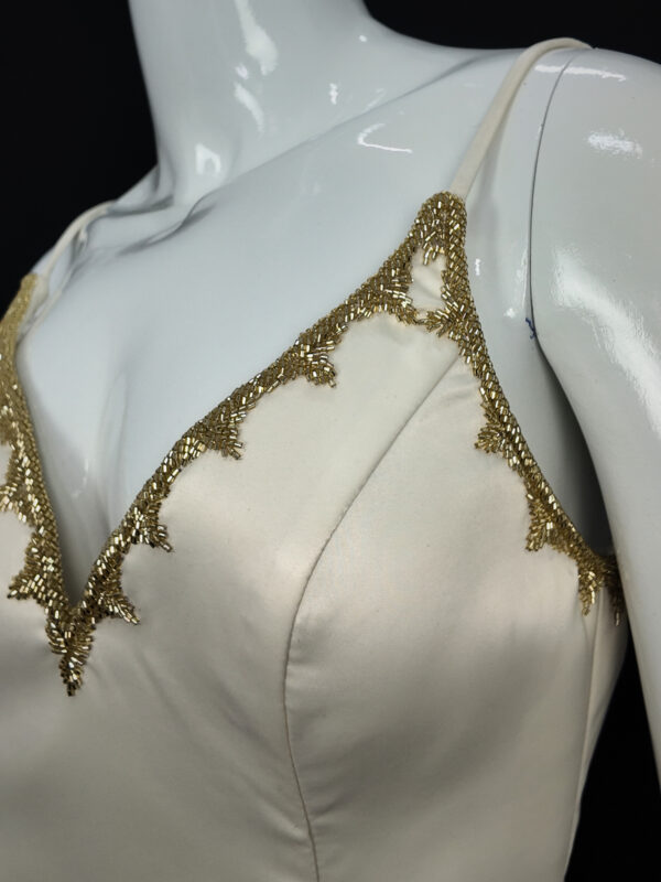 Close-up of the Gilded Venus bridal gown, highlighting intricate gold lace details and delicate beading on the bodice.